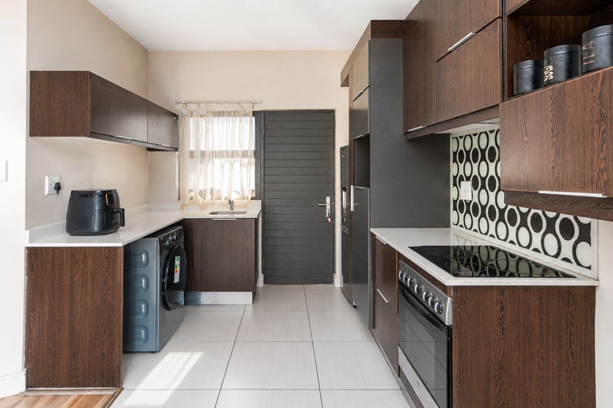 Modern kitchen featuring dark wood cabinetry, stone countertops, a built-in electric oven and hob, and a dedicated laundry area with plumbing connections.