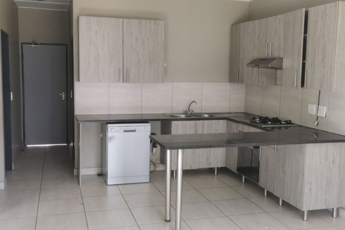 A functional kitchen featuring light wood-grain cabinetry, dark granite countertops, a built-in gas hob, extractor fan, and tiled flooring throughout.