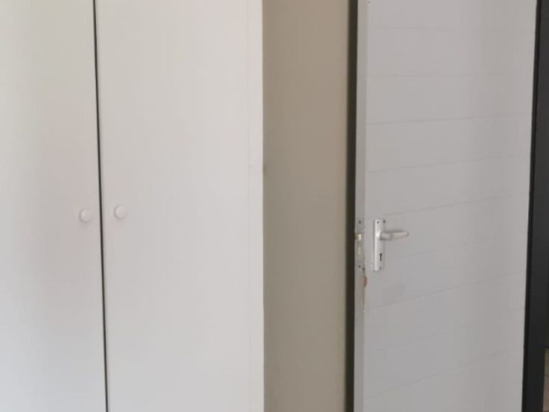 A bedroom interior featuring built-in white cupboards and a grey internal door with wood-look laminate flooring.