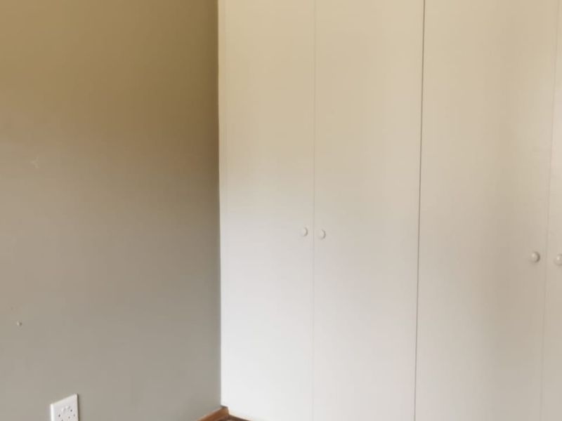 A bedroom interior featuring built-in cupboards with white doors and neutral wall finishes.