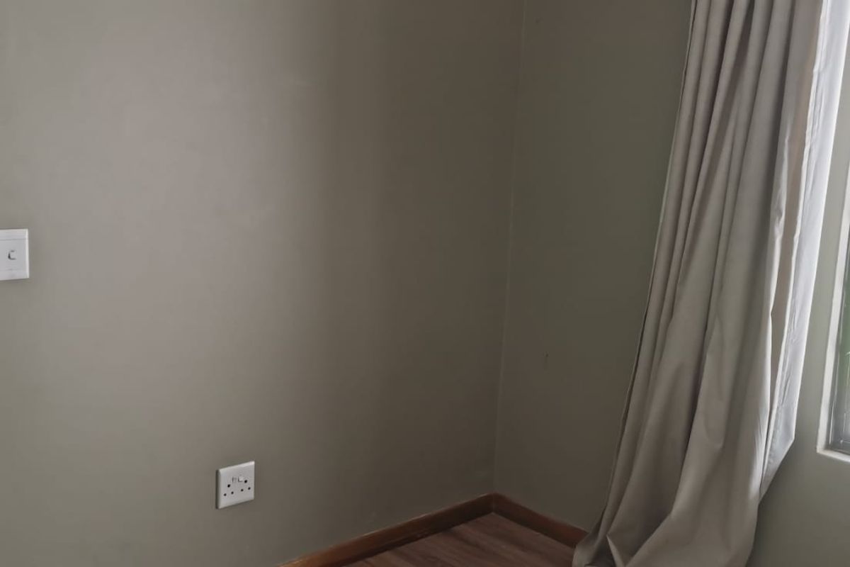 A bedroom featuring laminate flooring, a large window with security bars, and neutral wall tones, offering a clean and functional living space.