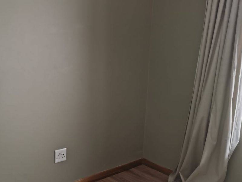 A bedroom featuring laminate flooring, a large window with security bars, and neutral wall tones, offering a clean and functional living space.