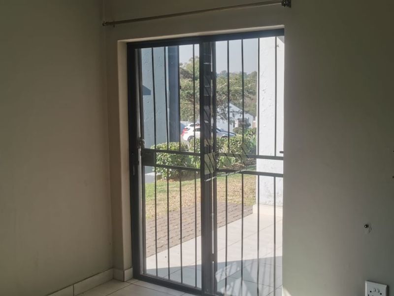 A vacant living area featuring tiled flooring, a sliding glass door with security gate, and a window with security bars.