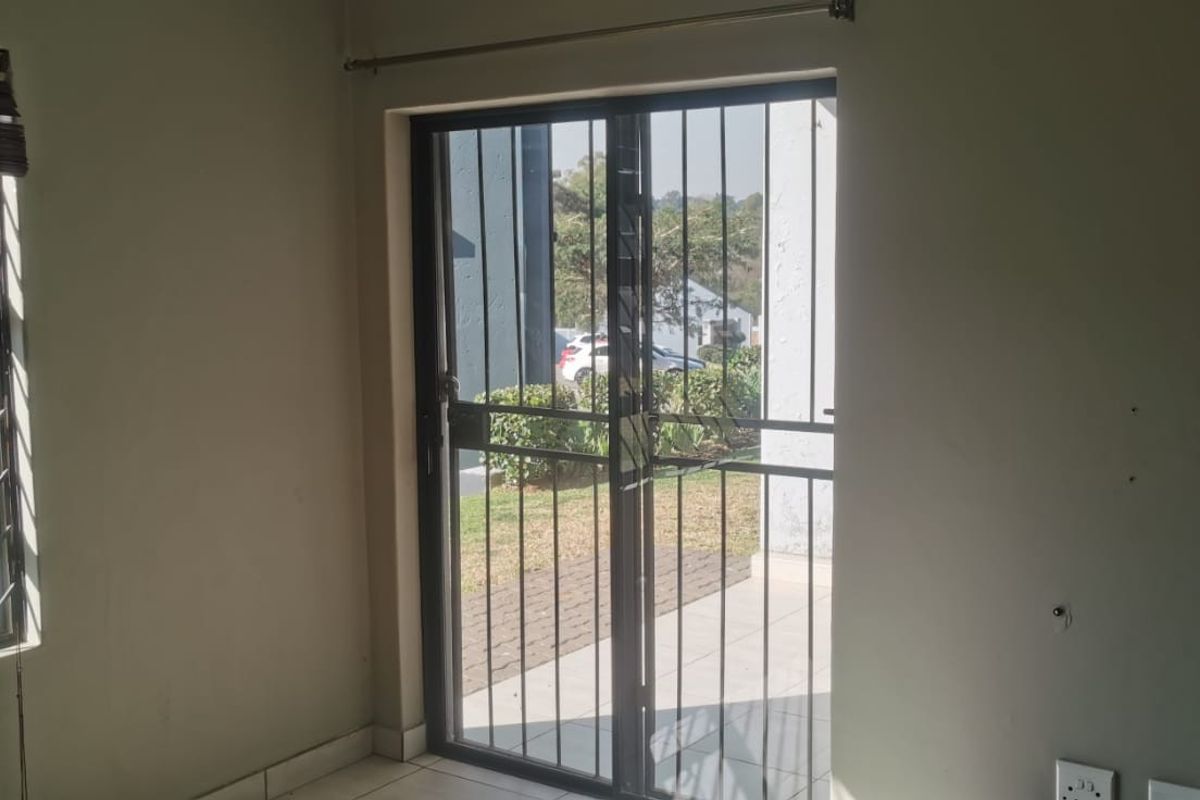 A vacant living area featuring tiled flooring, a sliding glass door with security gate, and a window with security bars.