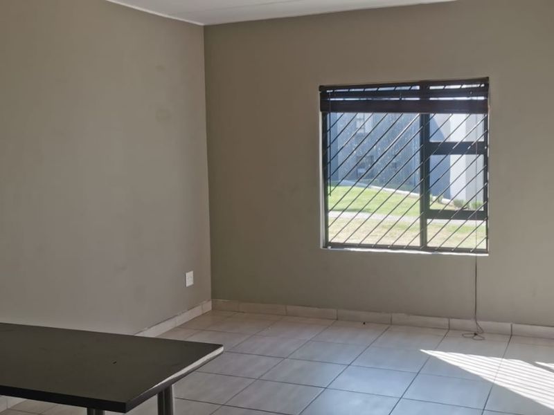An open-plan living area featuring tiled flooring, a large window with security bars, and a breakfast counter connecting to the kitchen space.
