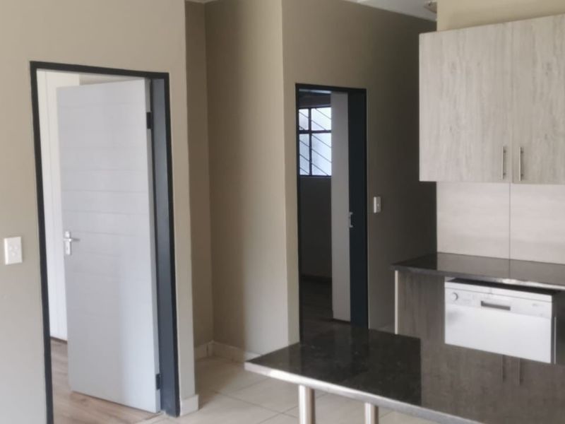 Modern open-plan kitchen featuring stone countertops, light wood-grain cabinetry, and integrated dishwasher space, seamlessly flowing into the adjacent living area.