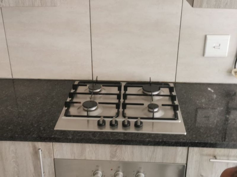 A modern kitchen featuring granite countertops, a built-in gas hob, and light wood-grain cabinetry with tiled splashbacks.
