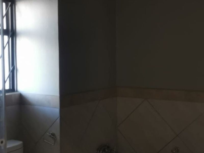 A functional bathroom featuring a built-in bathtub with tiled surround, a standard toilet, and a window with security bars.
