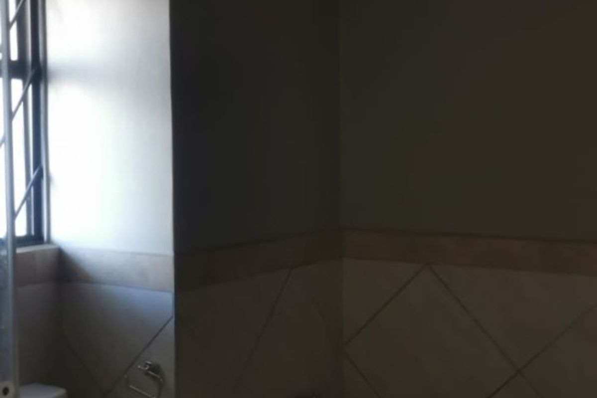 A functional bathroom featuring a built-in bathtub with tiled surround, a standard toilet, and a window with security bars.
