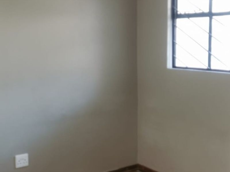 A vacant bedroom featuring wood-look laminate flooring, neutral wall paint, and a window fitted with security bars.