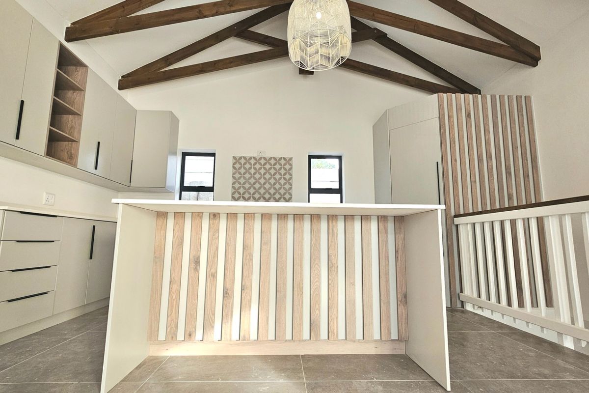 Modern kitchen featuring a central island with wood-slat detailing, exposed timber ceiling beams, and sleek cabinetry under a vaulted ceiling.