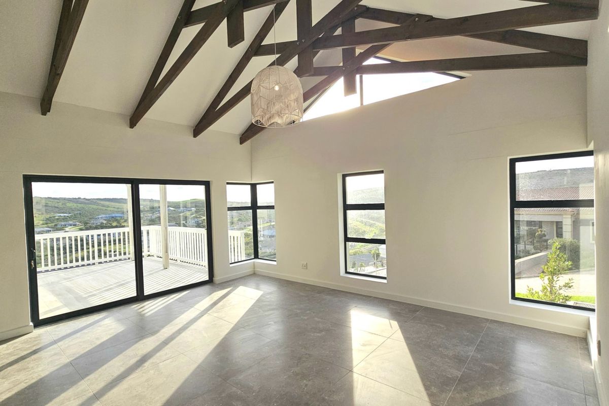 Spacious living area featuring high vaulted ceilings with exposed timber trusses, large windows, and sliding doors opening onto a balcony with scenic views.