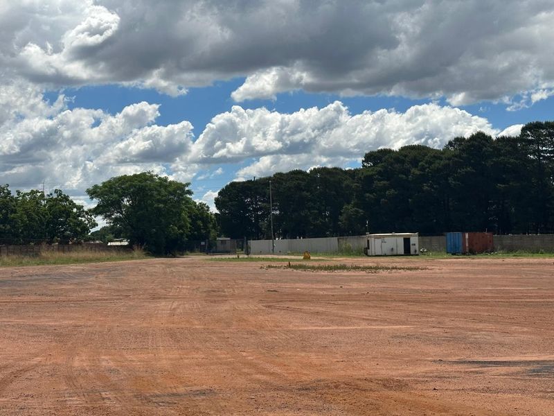 Expansive industrial yard space featuring unpaved ground, perimeter walling, and basic utility structures, suitable for storage or industrial development.