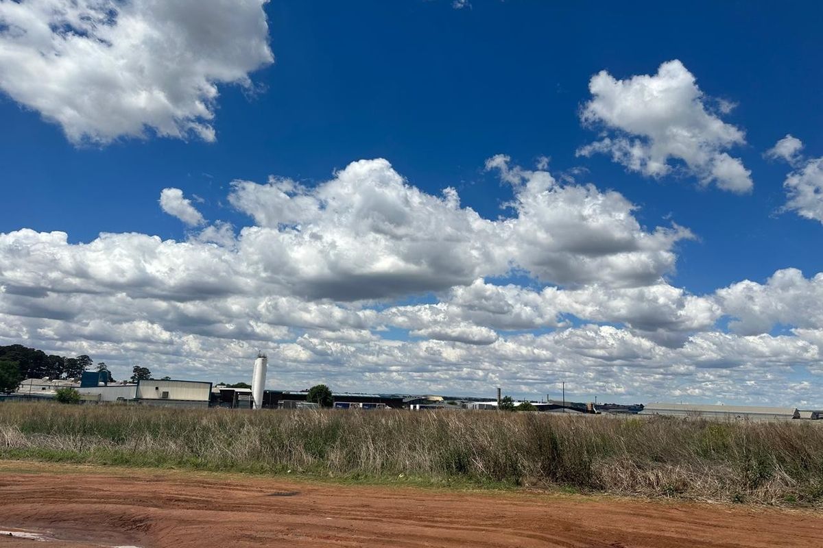 A wide-angle view of an industrial site featuring large warehouse structures, a silo, and surrounding open land under a clear blue sky.
