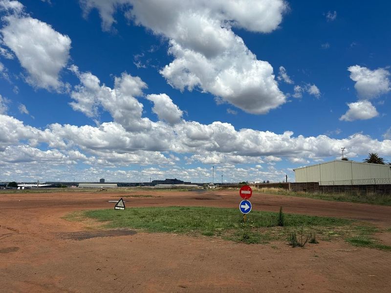 Expansive industrial yard area featuring unpaved ground, perimeter fencing, and basic traffic signage under a clear sky.