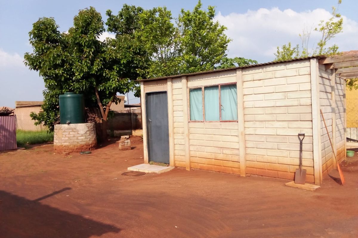 A detached outbuilding constructed of concrete blocks with a corrugated metal roof, featuring an adjacent water storage tank in a rural yard setting.