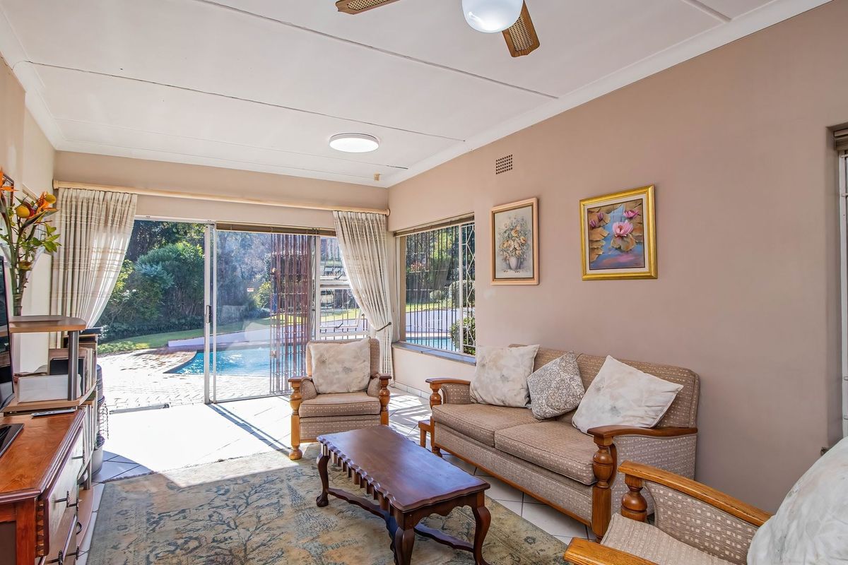 A bright living room featuring tiled flooring, a ceiling fan, and large sliding glass doors that provide direct access to the outdoor pool area.