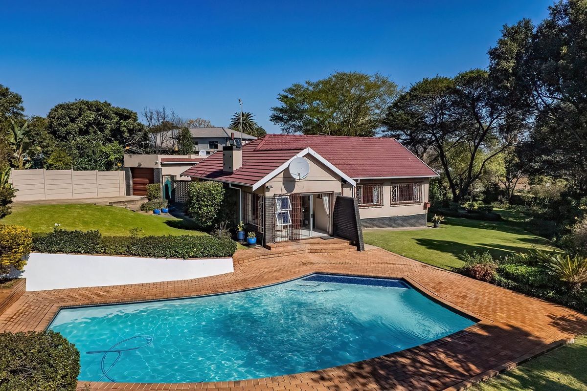 Aerial view of the rear exterior featuring a swimming pool, brick paved patio area, and a well-maintained garden surrounding the house.