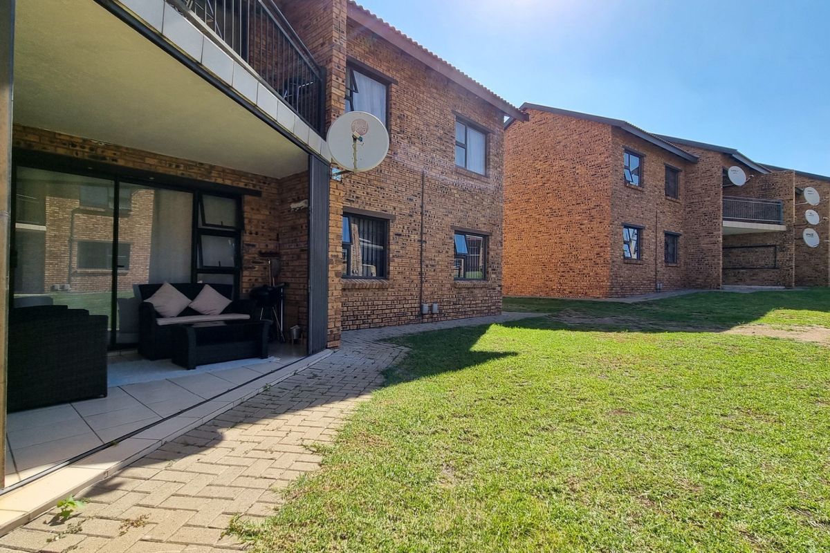 Exterior view of a brick apartment complex featuring a ground-floor patio area and shared garden space.