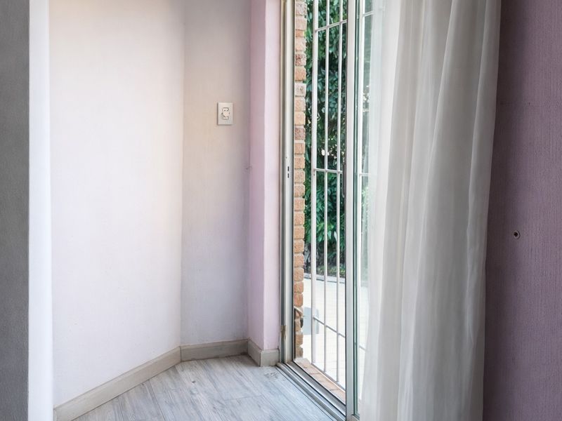 A small interior space featuring light wood-look flooring and a sliding glass door with security bars, providing access to an outdoor area.