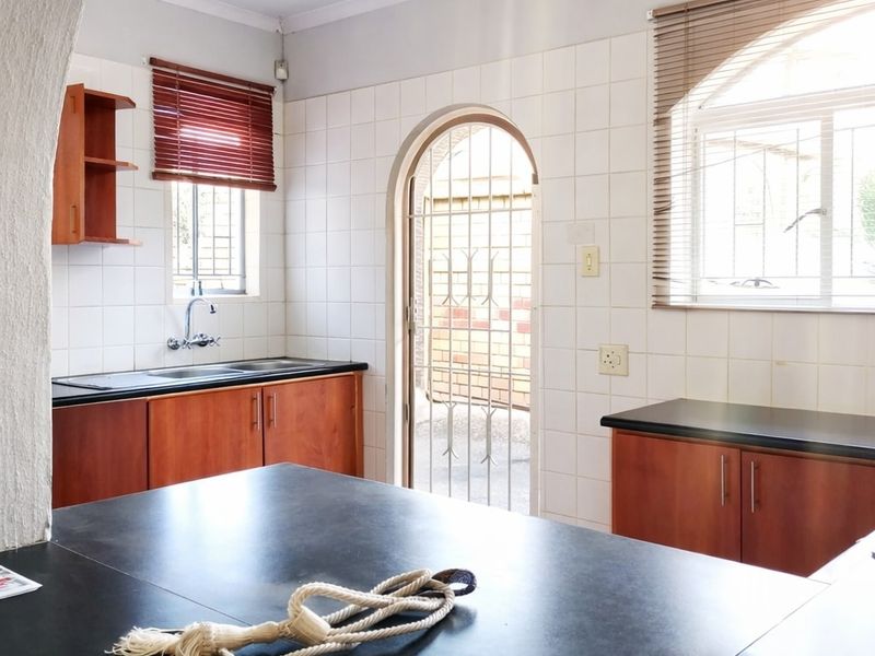 A functional kitchen featuring wooden cabinetry, dark countertops, tiled splashbacks, and an arched doorway leading to an exterior area.