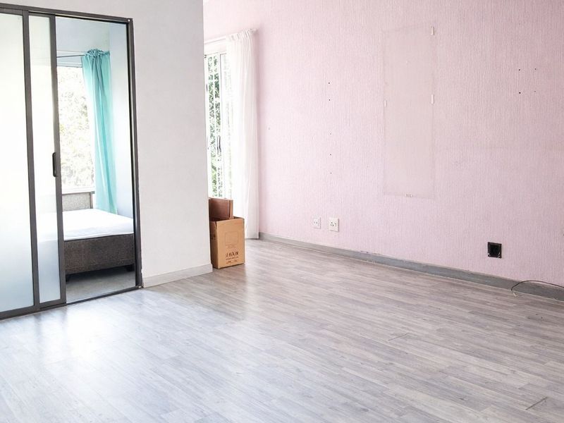 An empty living room featuring light wood-look flooring, a textured pink accent wall, and a sliding glass door leading to an adjacent bedroom.