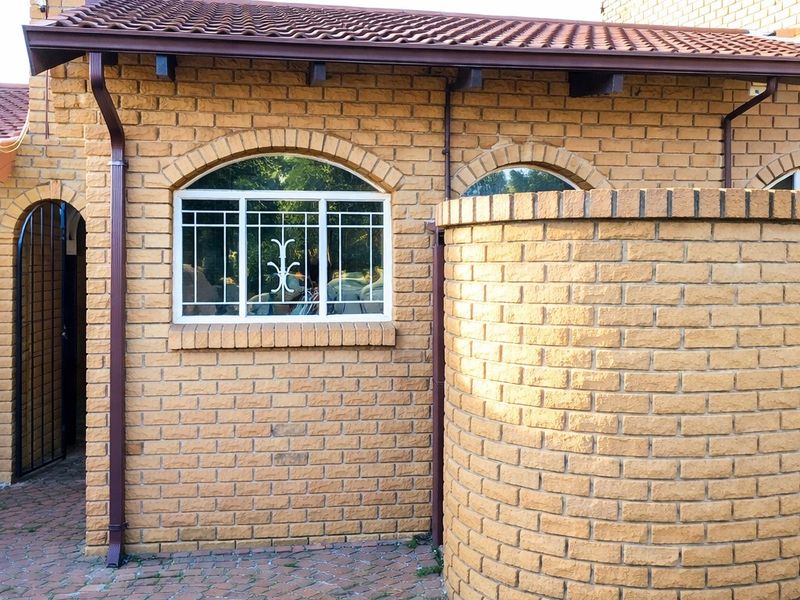 A view of the exterior rear facade featuring face brick construction, arched window frames with security bars, and a paved courtyard area.