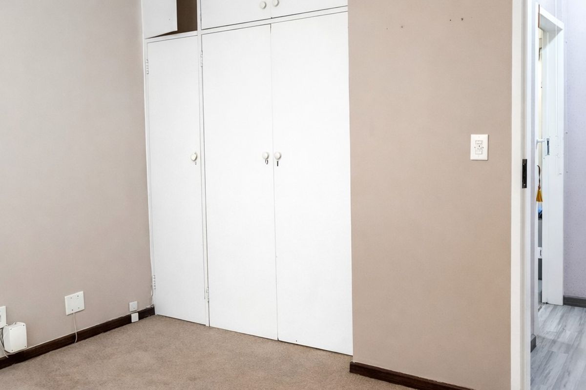 A vacant bedroom featuring built-in cupboards with overhead storage and neutral wall finishes, leading into an adjacent hallway.