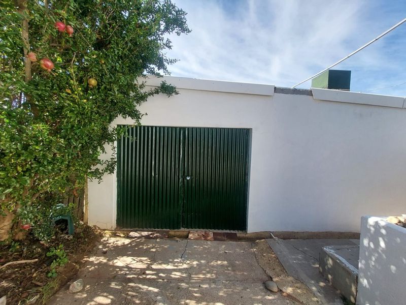 Exterior view of a garage featuring a dark green corrugated metal door and a white rendered facade.