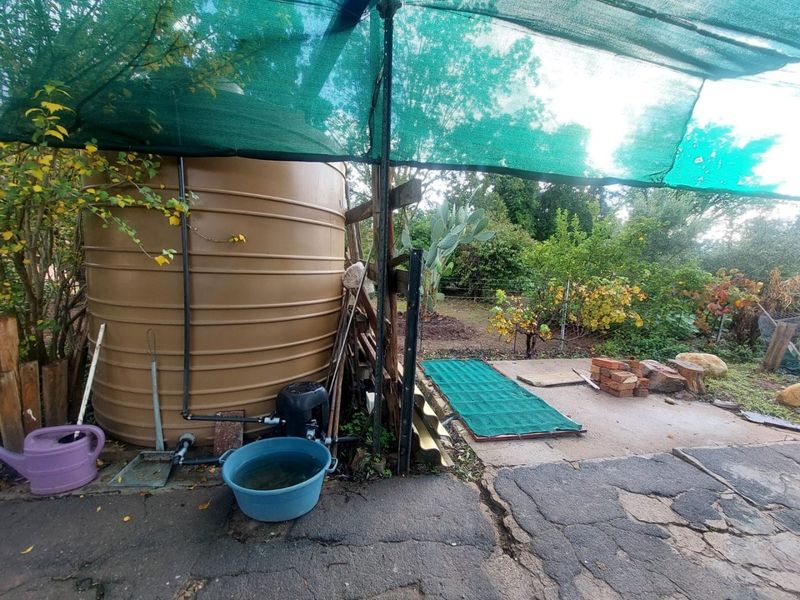 Outdoor utility area featuring a large water storage tank, pump system, and shade cloth covering over a paved surface.
