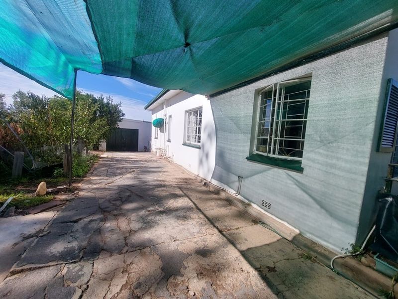 Exterior view of the side driveway featuring a large shade cloth canopy, security bars on windows, and access to a detached garage.