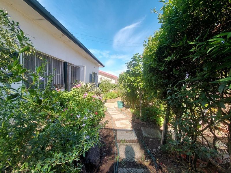 A side garden path featuring established greenery and a paved walkway leading along the side of the house.