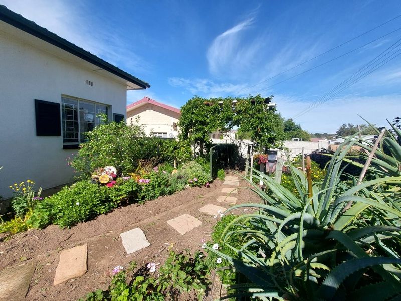 A landscaped garden path featuring stone pavers, established greenery, and a wooden pergola leading through the side yard of the property.