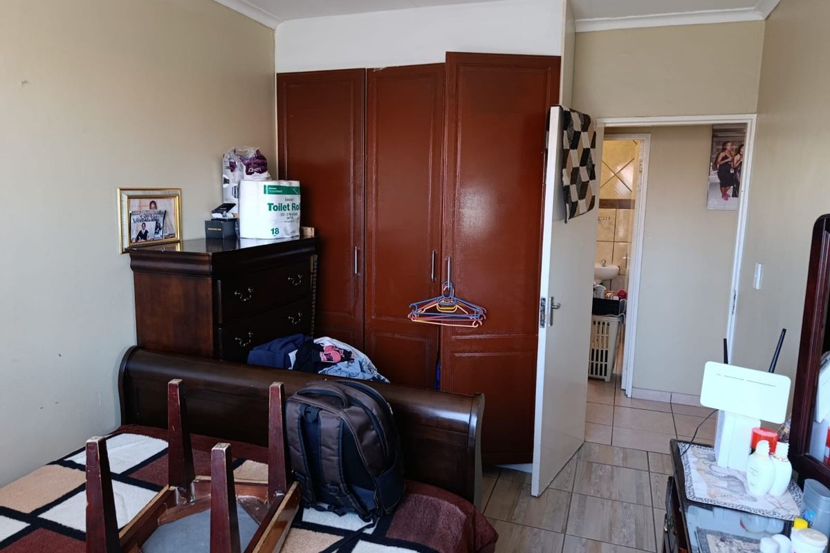 A bedroom featuring built-in wooden cupboards and tiled flooring, with an adjacent doorway leading to a bathroom area.