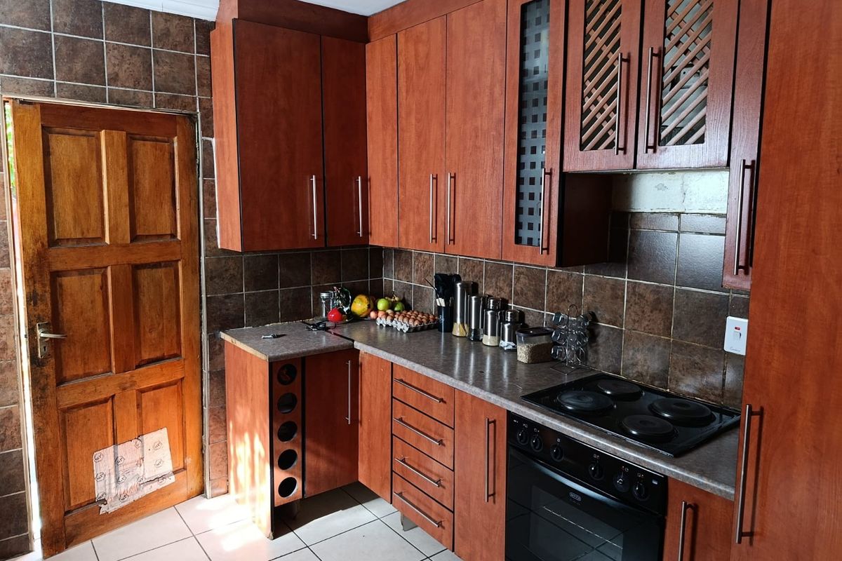 A functional kitchen featuring wood-veneer cabinetry, a built-in electric oven and hob, dark tiled backsplash, and tiled flooring with direct exterior access.