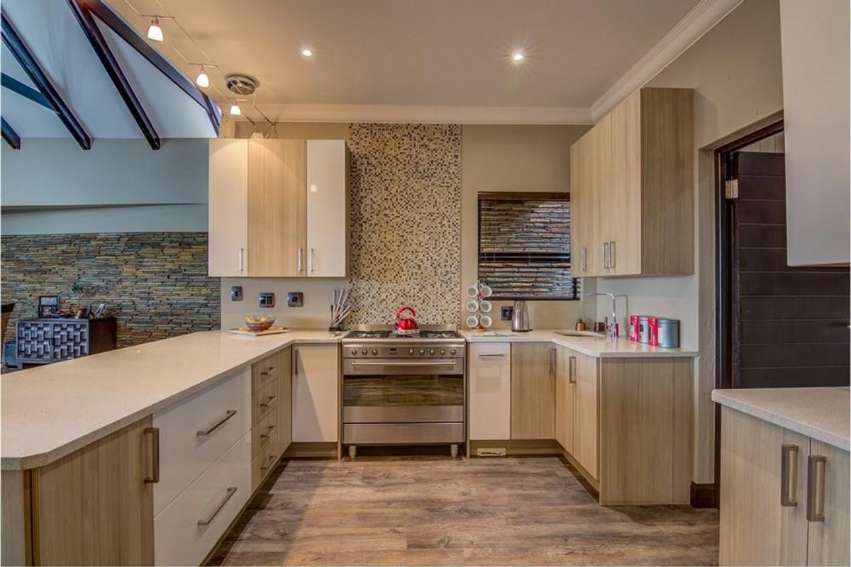Modern kitchen featuring light wood cabinetry, stone-look countertops, a stainless steel gas stove, and a decorative mosaic tile backsplash.