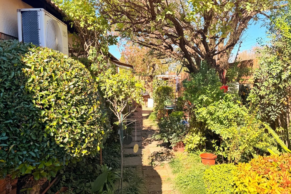 A view of the rear garden area featuring established trees, paved pathway, and wall-mounted air conditioning unit.