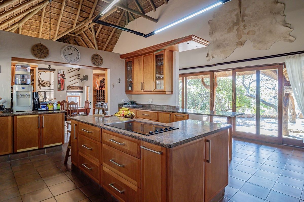 Spacious kitchen featuring wooden cabinetry, granite countertops, a central island with a built-in hob, and high vaulted thatched ceilings with exposed timber trusses.