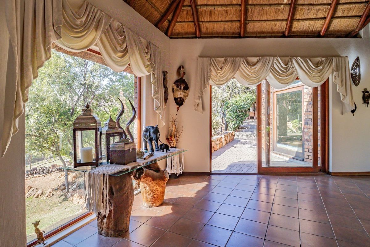 Spacious living area featuring a traditional thatched roof with exposed timber rafters, ceramic tiled flooring, and large windows providing natural light and garden views.