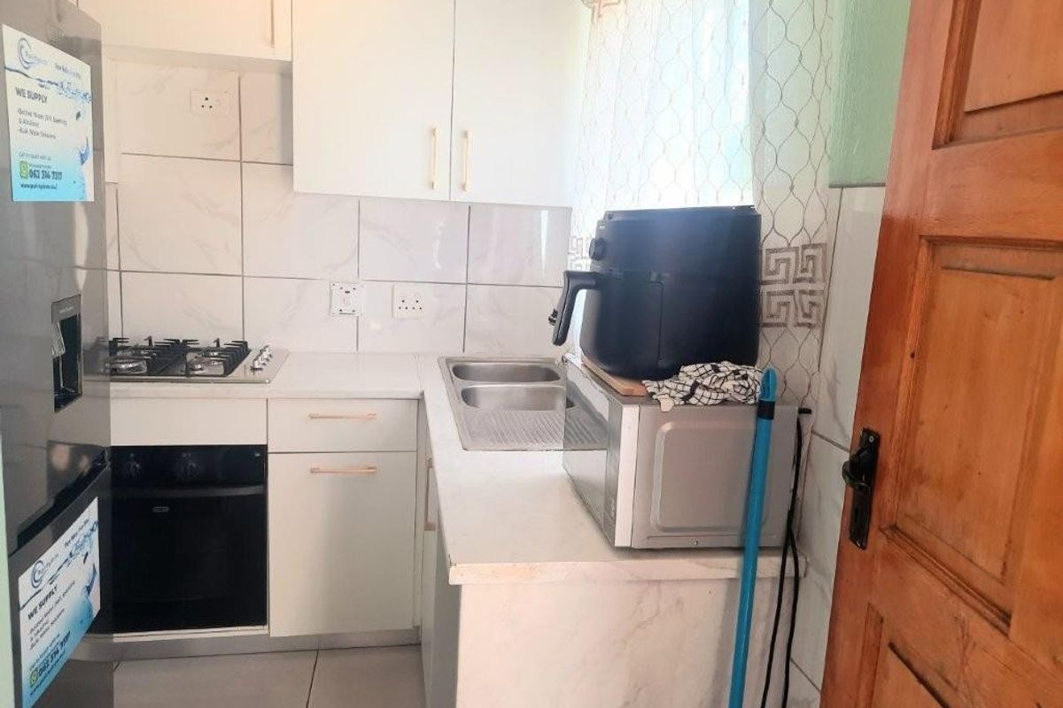 Compact kitchen featuring built-in cabinetry, a gas hob, an under-counter oven, and a double-basin stainless steel sink with tiled splashbacks.