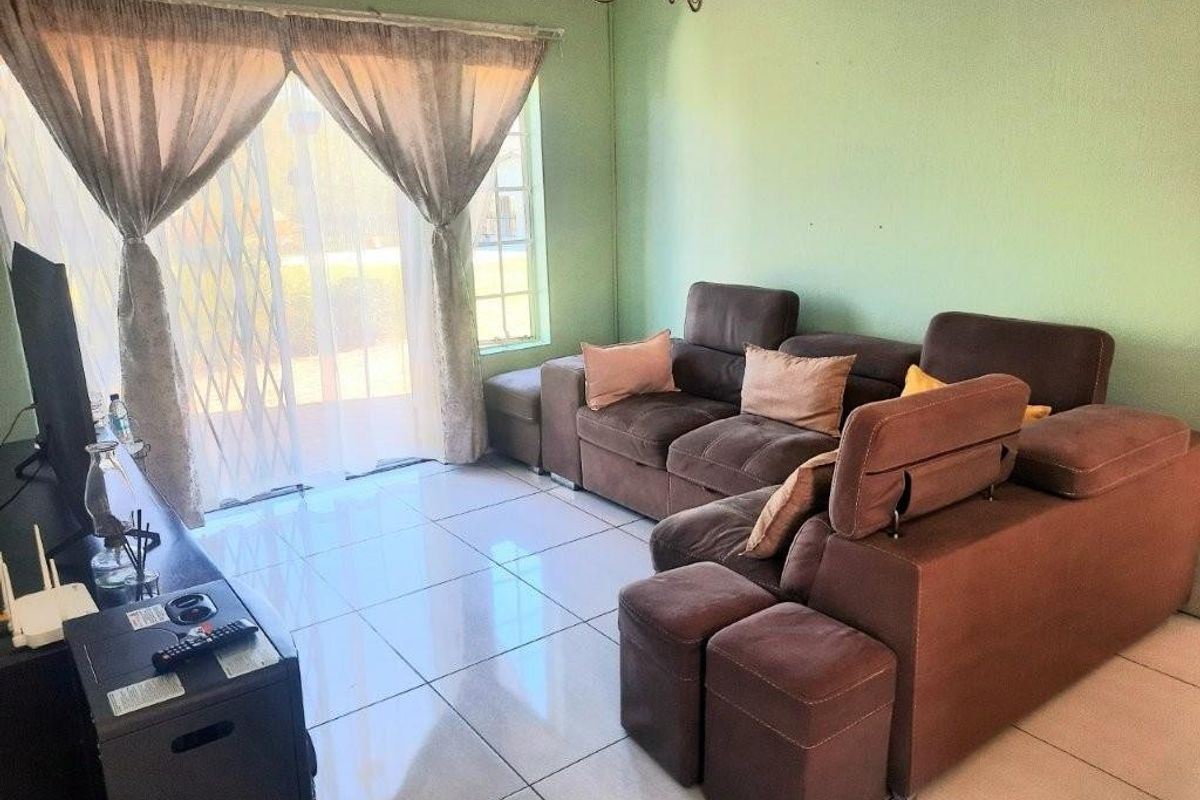 A living room featuring large format floor tiles and a sliding glass door with security gate, providing access to the exterior.
