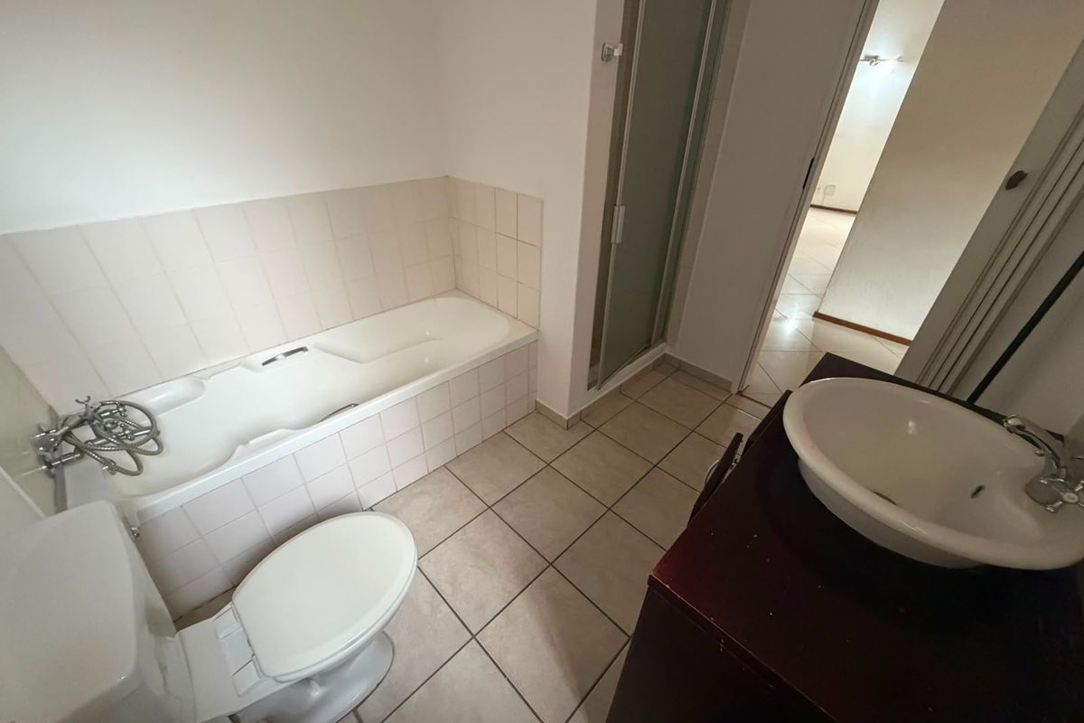 A functional bathroom featuring a built-in bathtub with tiled surround, a separate shower enclosure, a toilet, and a vanity basin.