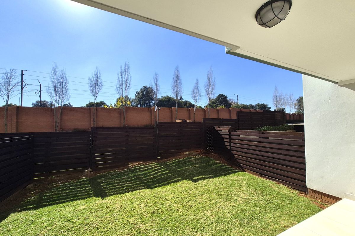 A private rear garden area featuring a small lawn, enclosed by dark timber slat fencing and a brick boundary wall.