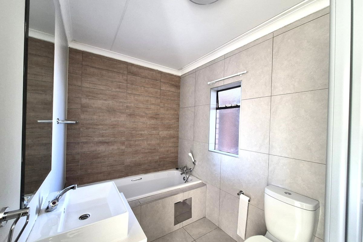 Modern bathroom featuring a tiled bathtub, vessel sink vanity, and a toilet with neutral wall and floor tiling.