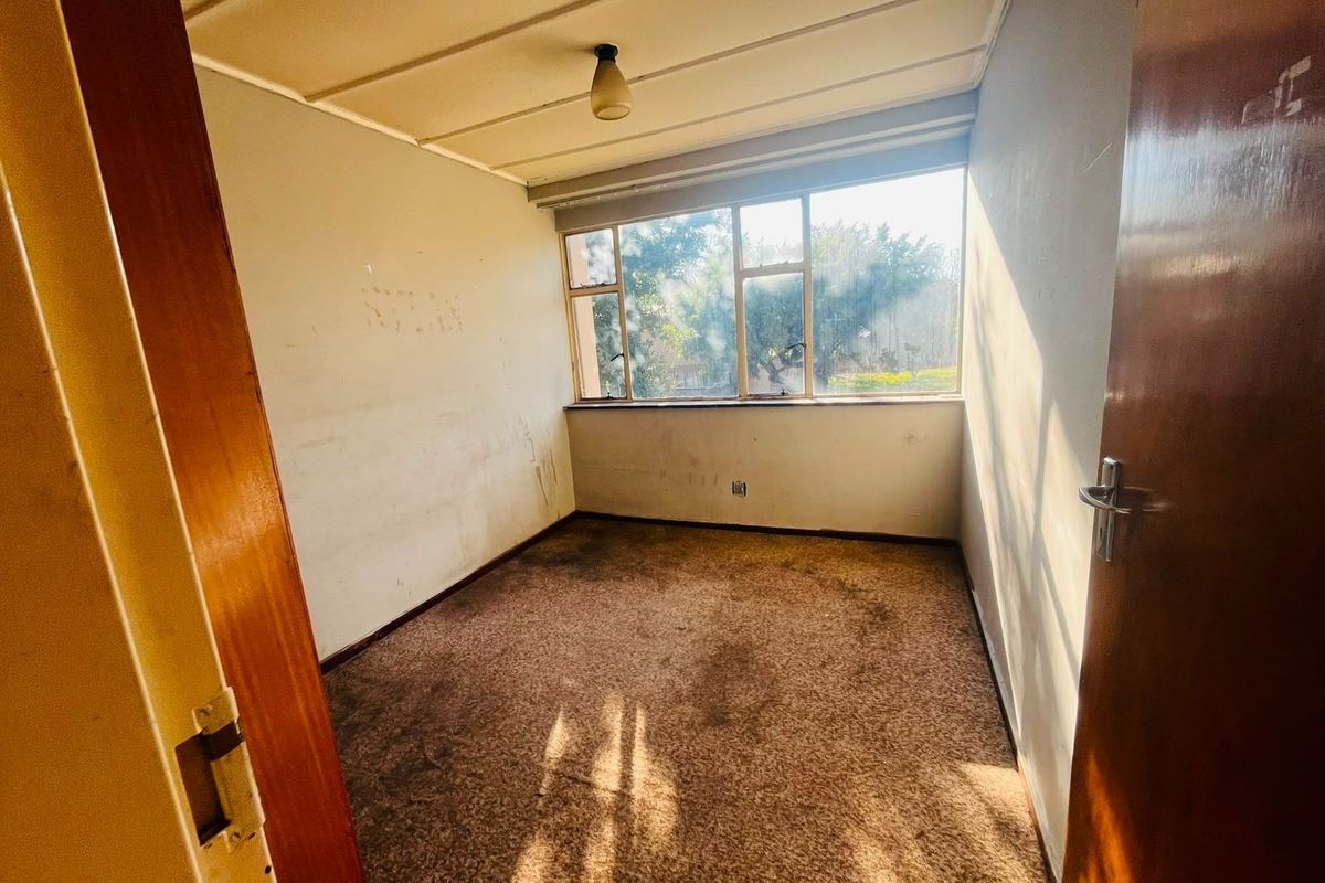 A vacant bedroom featuring worn carpeting, marked walls, and a large window providing natural light.