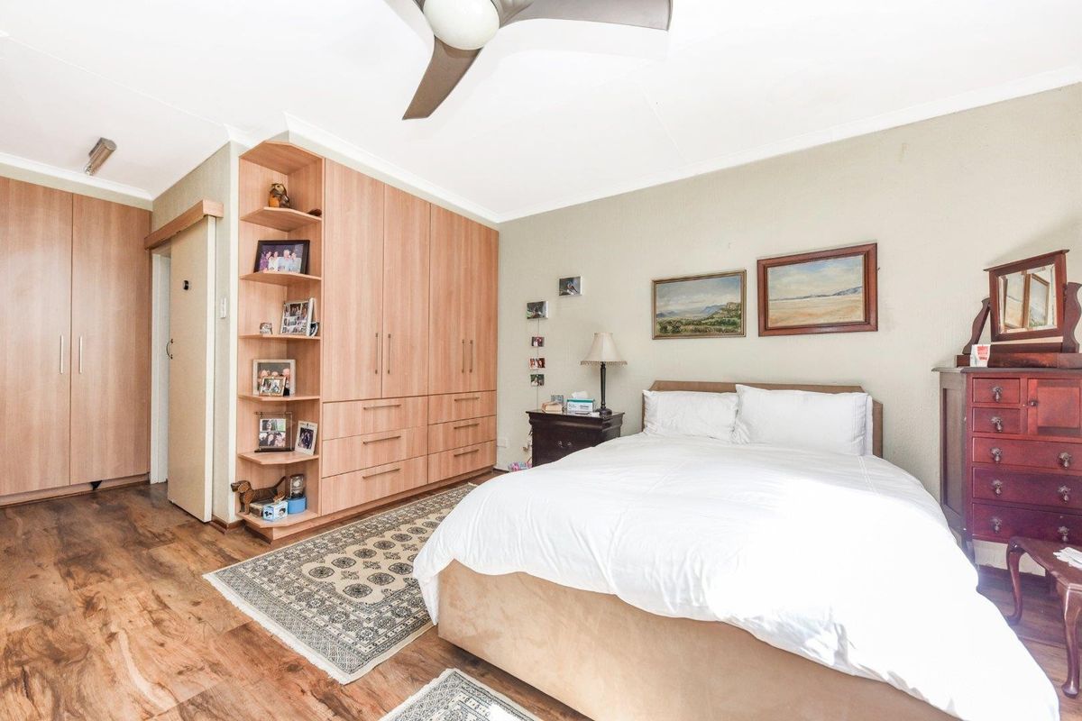 A well-proportioned bedroom featuring built-in wooden cabinetry with integrated shelving, laminate flooring, and a ceiling fan.