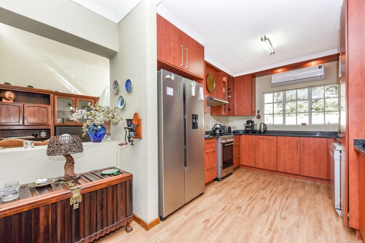 A functional kitchen featuring wood-finish cabinetry, dark countertops, a built-in oven with extractor fan, and a wall-mounted air conditioning unit.