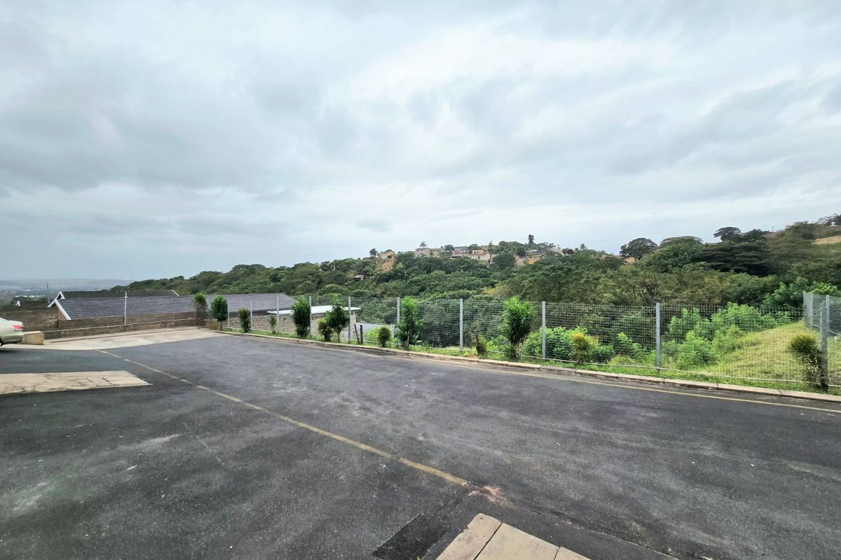 An outdoor area featuring an asphalt driveway, wire mesh perimeter fencing, and a view overlooking a green hillside landscape.