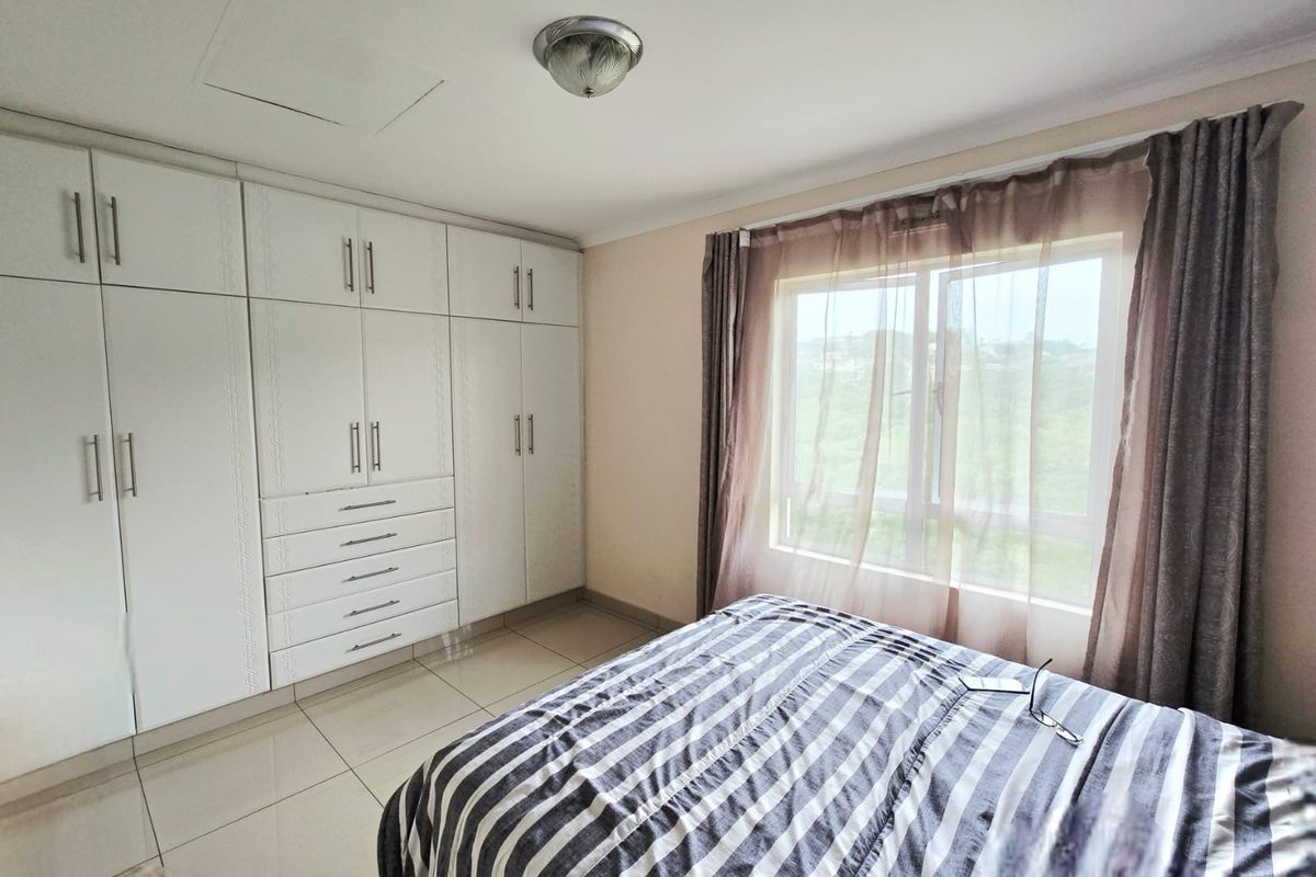 A well-maintained bedroom featuring extensive built-in white cabinetry, neutral tiled flooring, and a large window allowing for natural light.