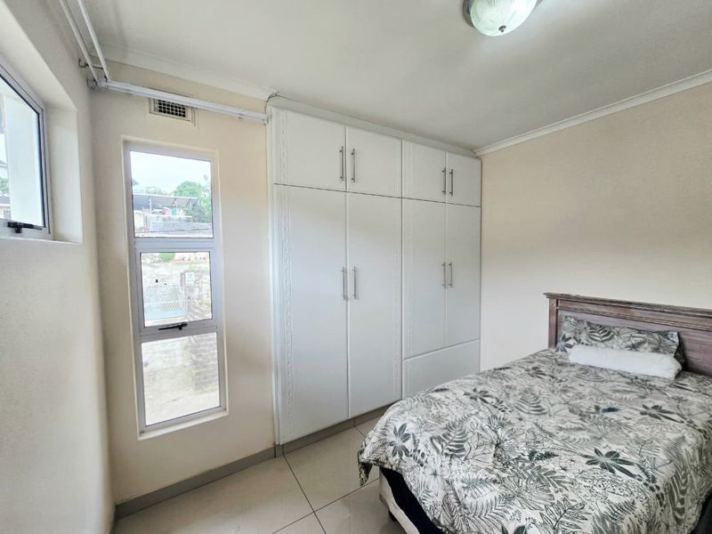 A well-maintained bedroom featuring neutral tiled flooring, ample built-in cupboard storage, and natural light through aluminium-framed windows.